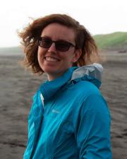 A woman with a raincheck and glasses standing on the beach, smiling